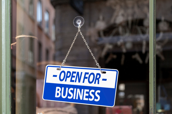 Shop door with a sign hanging in it saying 'Open for business'