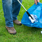 person holding a litter picker and rubbish bag, collecting litter from grass