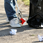 person holding a litter picker and black rubbish bag, collecting litter from grass