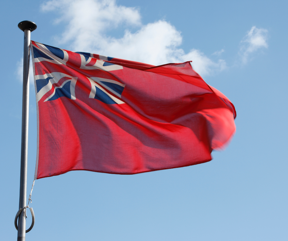 The Red Ensign Flag ( red background with the Union Jack in the top left corner) raised on a flagstaff with a clear blue sky in the background