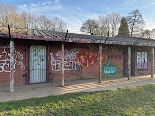 old disused small red brick building with colourful graffiti in a green open space park