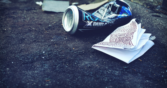 Crushed can and a piece of paper with doodles on dropped on road.