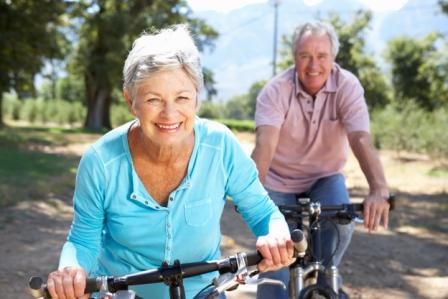 eldery male and female riding cycles in the sunshine through a park