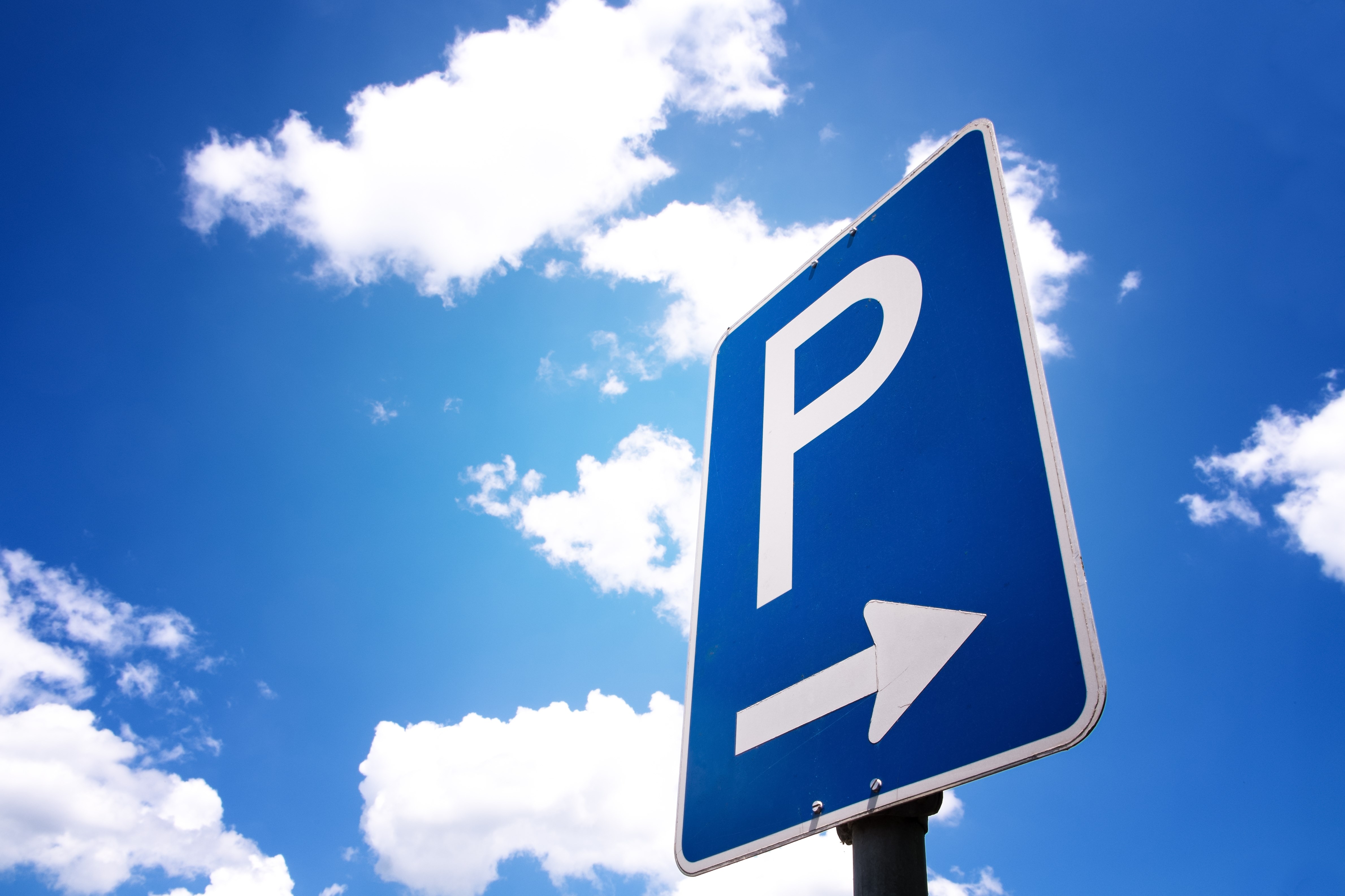 Parking sign with arrow. Blue sky and clouds in background.