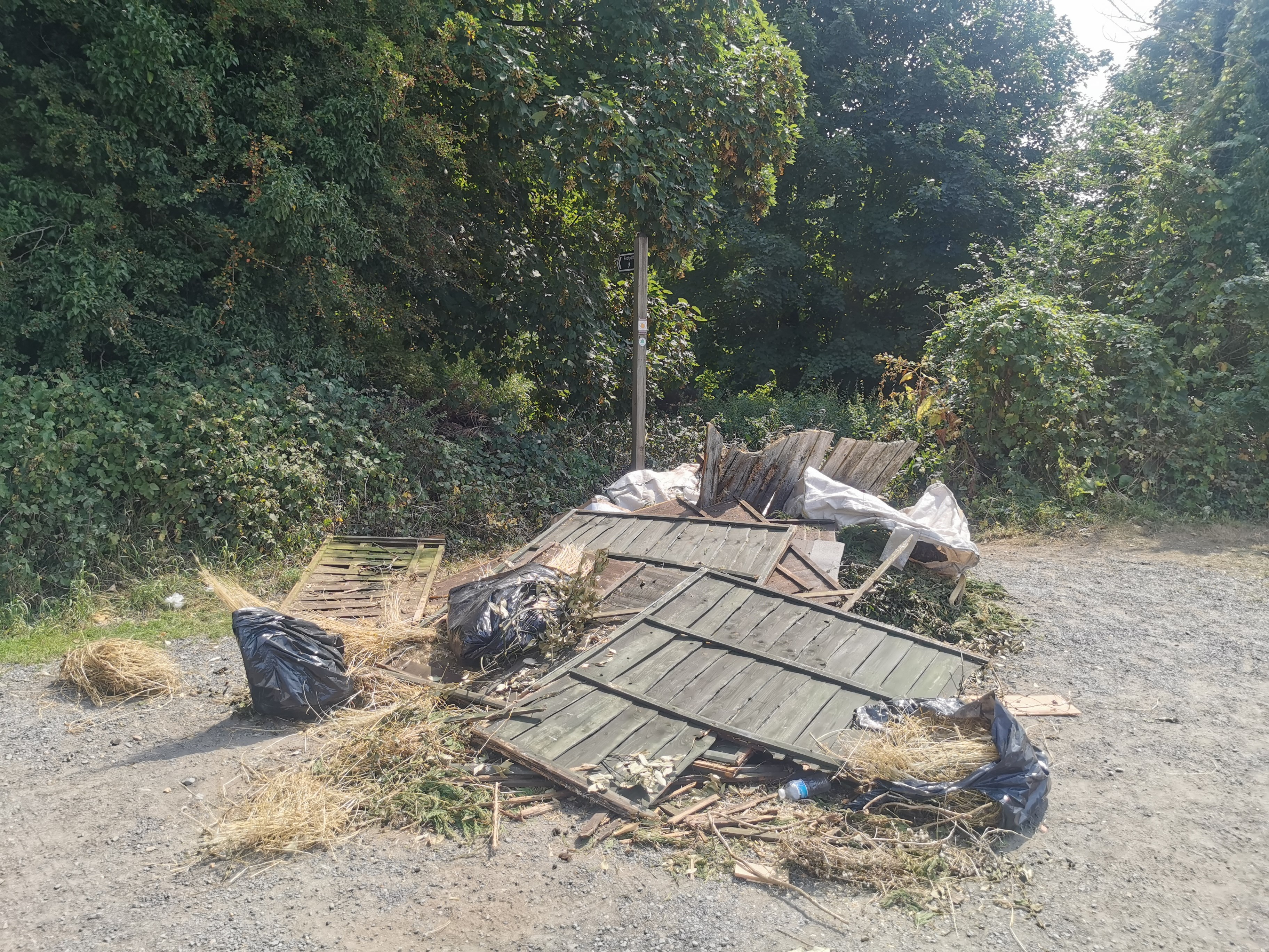 dumped (flytipped) rubbished containing old broken fence panels, black bags, and garden rubbish in a rural area