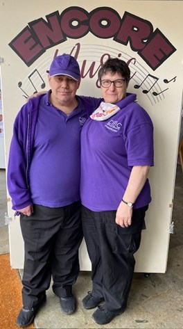 2 people in purple shirts in front of sign that reads encore