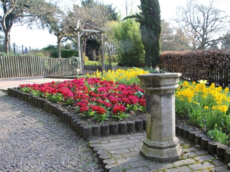a cobbled footpath is lined with brightly coloured summer bedding plants and the parks sundial