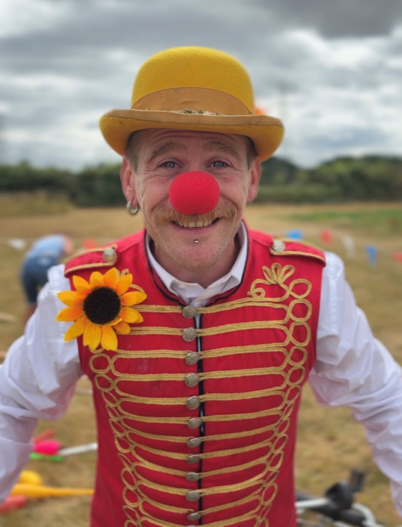 Photo of Lee the one man circus show. he is wearing a yellow bowler hat and yellow and red stripy waistcoat on which is pinned a yello sunflower. He has a big fake red nose.
