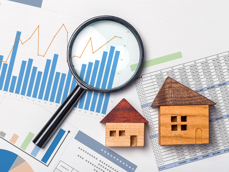 Wooden model houses and a magnifying glass on top of papers with graphs on