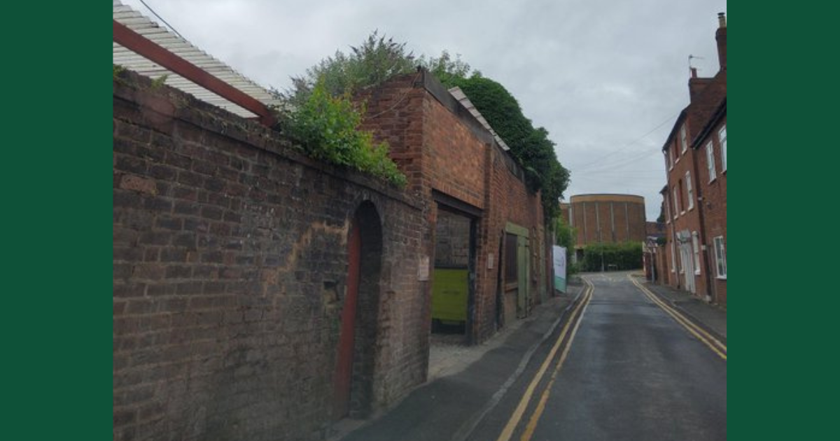 Image of a street. Focus is on a brick wall which is leaning into the road.