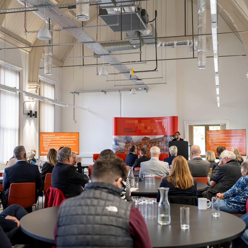 A presentation to a room of people sat around round tables