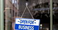 Shop door with a sign hanging in it saying 'Open for business'