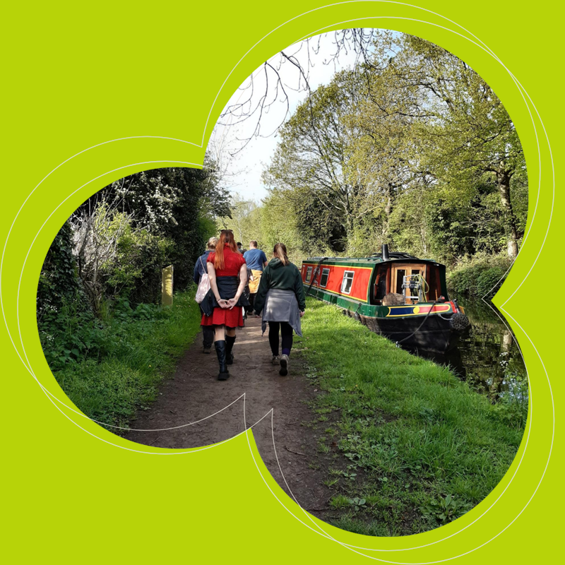 two people walking down a canal path with a canal boat to the right