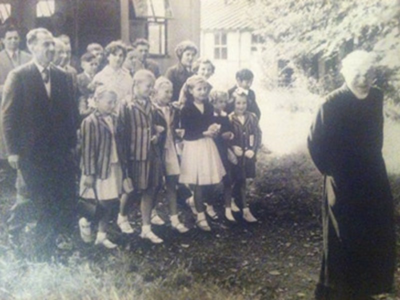 old grainy black and white photo of group of people standing in front of building a man in black robes stands in front of the group