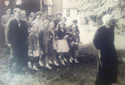 sepia image of group of adults and children with man in black robes just in front