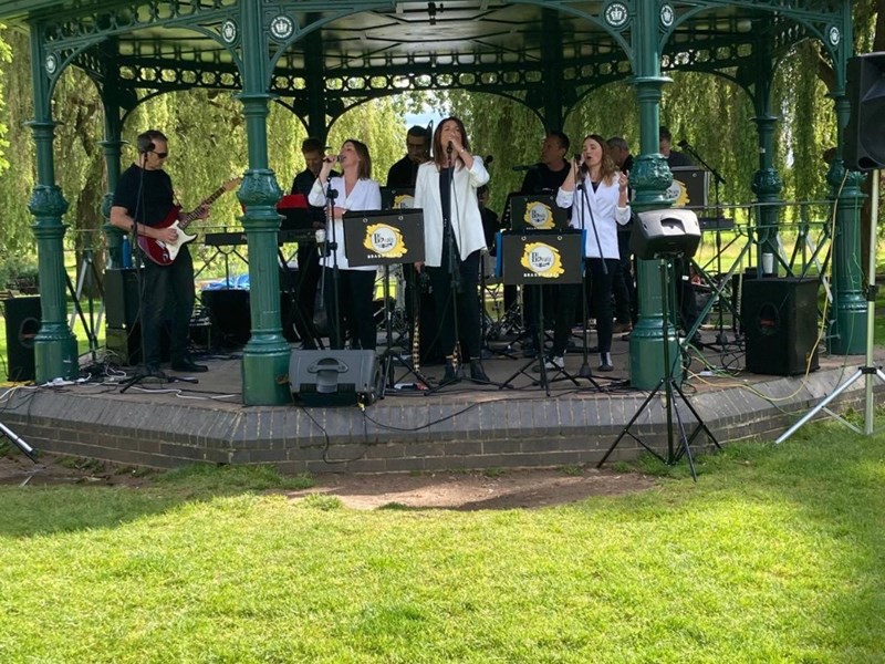 Image of the the band called Brass Beatz performing in a bandstand at a park with grass in front and trees behind