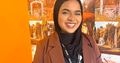 Young woman with head-covering smiling and standing in front of an orange background with Wyre Forest images on it.