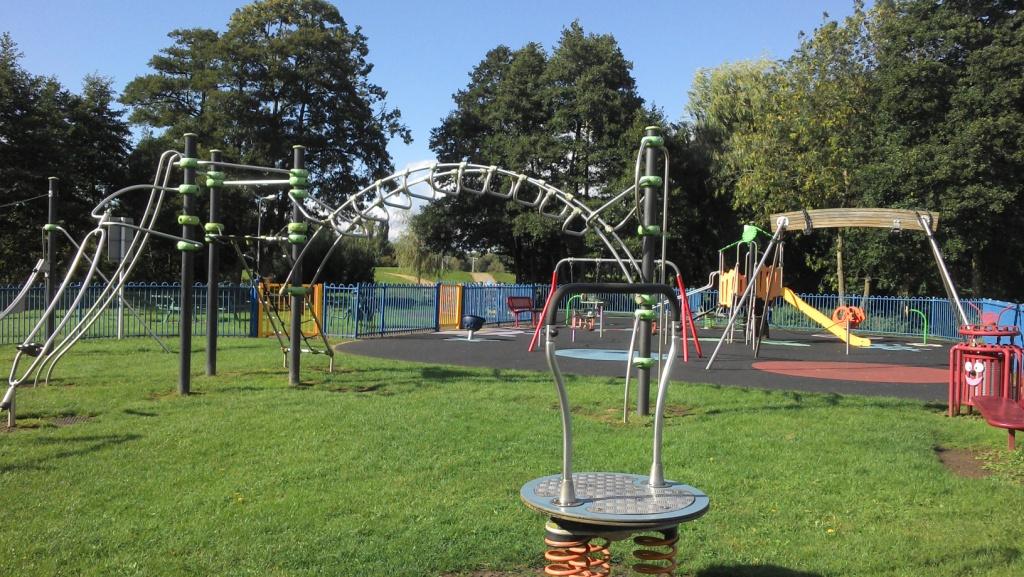 A childrens play area with brightly coloured climbing frames on a soft surface area within the public park area.