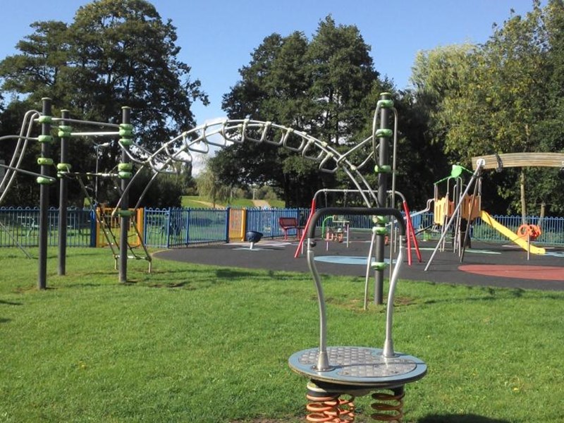 A childrens play area with brightly coloured climbing frames on a soft surface area within the public park area.