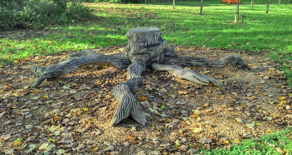 A tree stump sculpture created from a mature tree trunk cout low to the ground within the grassed area of the ublic gardens.