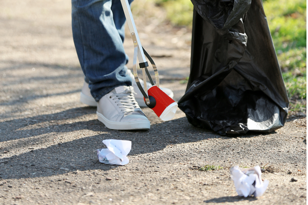 person holding a litter picker and black rubbish bag, collecting litter from grass