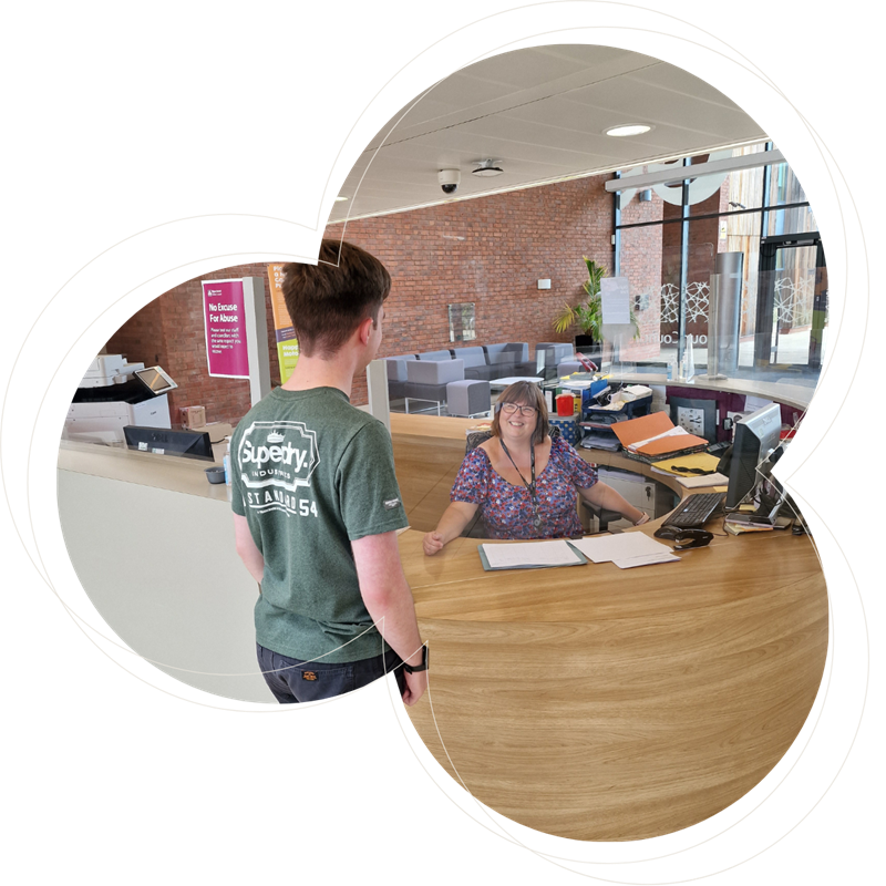 a male stood at a reception desk with a female receptionist smiling back