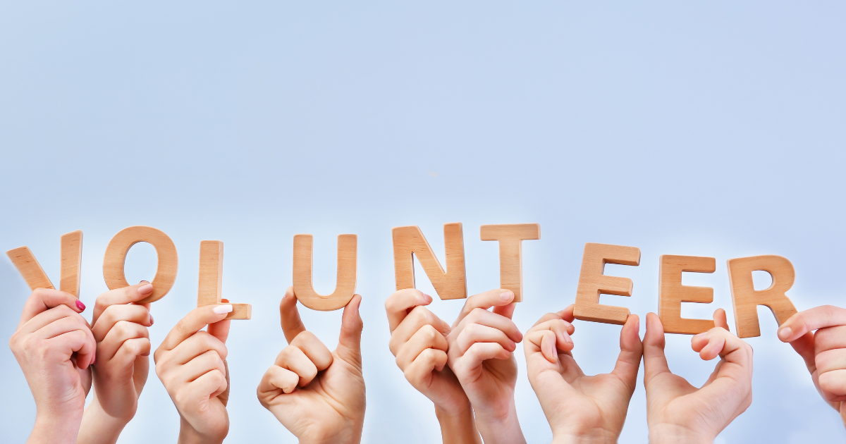 Hands on a blue background holding up wooden letters which spell "volunteer"