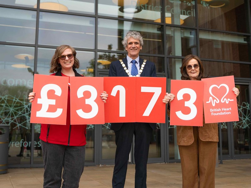 two females a male stood holding red signs with numbers on to represent how much money had been raised for the charity