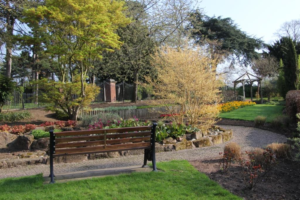 Park bench located in the park's sensory garden with flower borders and mature trees in the distance.