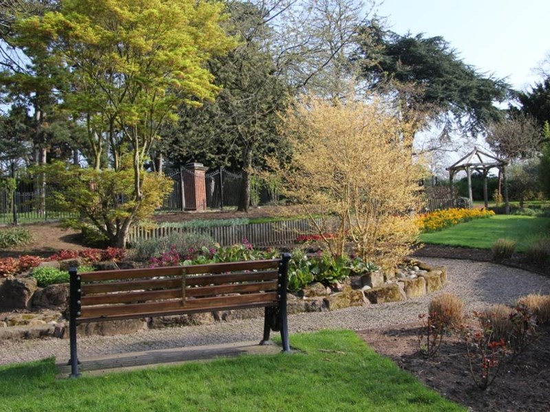 Park bench located in the park's sensory garden with flower borders and mature trees in the distance.