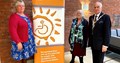 A pull up banner with No Barriers logo, a symbol of a person in a wheelchair, with one grey haired person stood to the left and two greyhaired people stood to right, one is wearing a chain of office