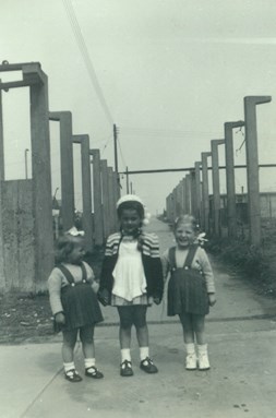 3 children in dresses at end of  concrete path with concrete uprights behind them