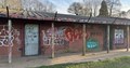 old disused small red brick building with colourful graffiti in a green open space park
