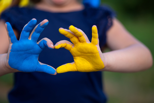 childs hands one painted blue the other yellow form a heart shape with thumbs and forefingers