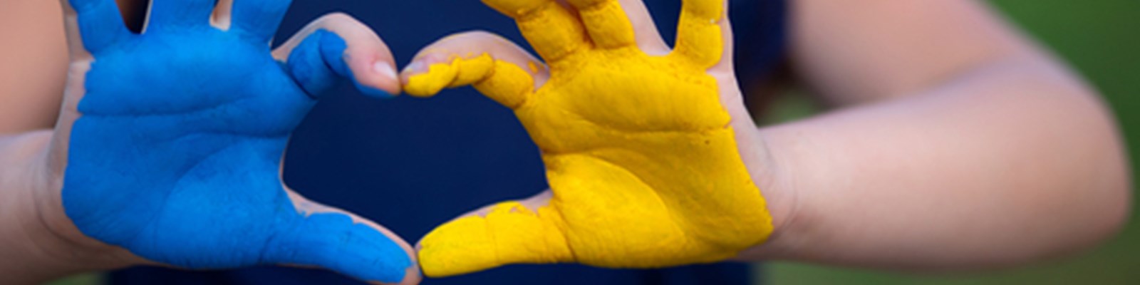 childs hands one painted blue the other yellow form a heart shape with thumbs and forefingers