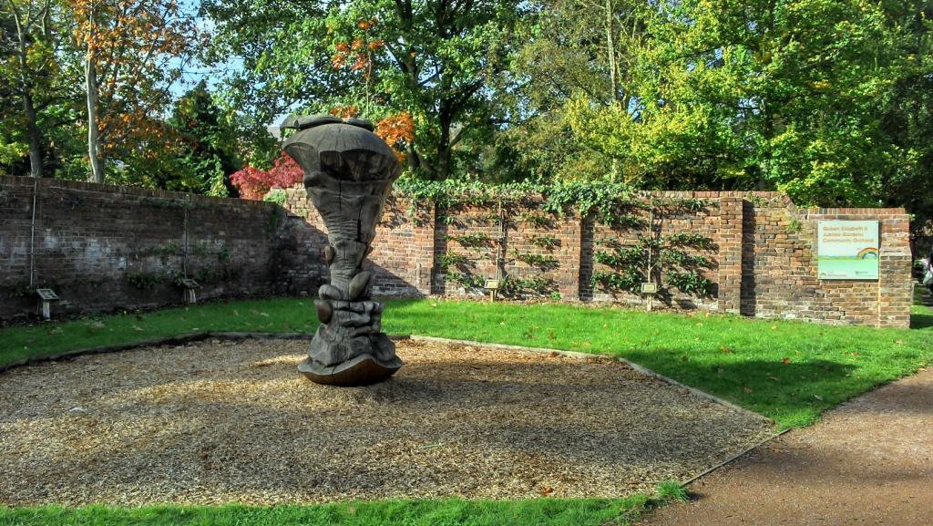 An area of the public gardens where a wooden apple core sculpture has been crafted from an old tree trunk.