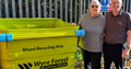 Two people stood next to a large lime green business waste container