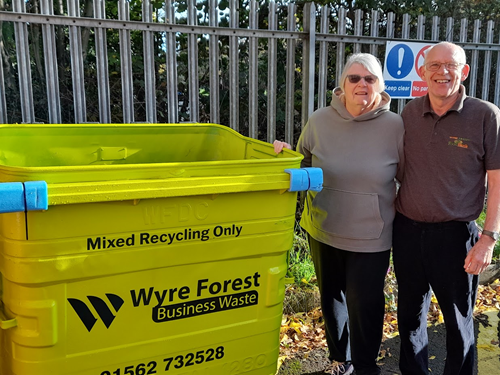 Two people stood next to a lime green recycling business waste bin