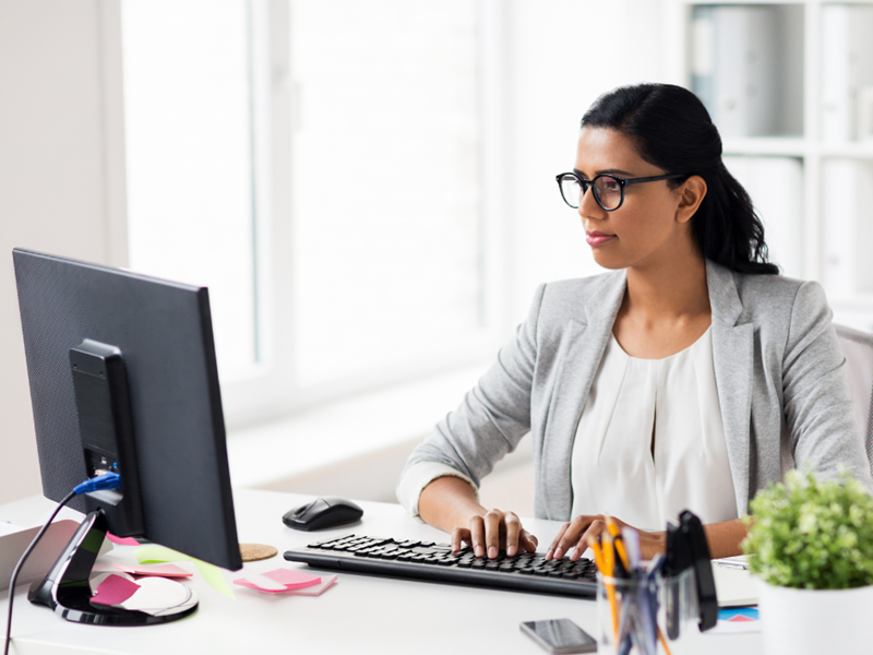 A woman in business wear sat at a desk using a desktop computer