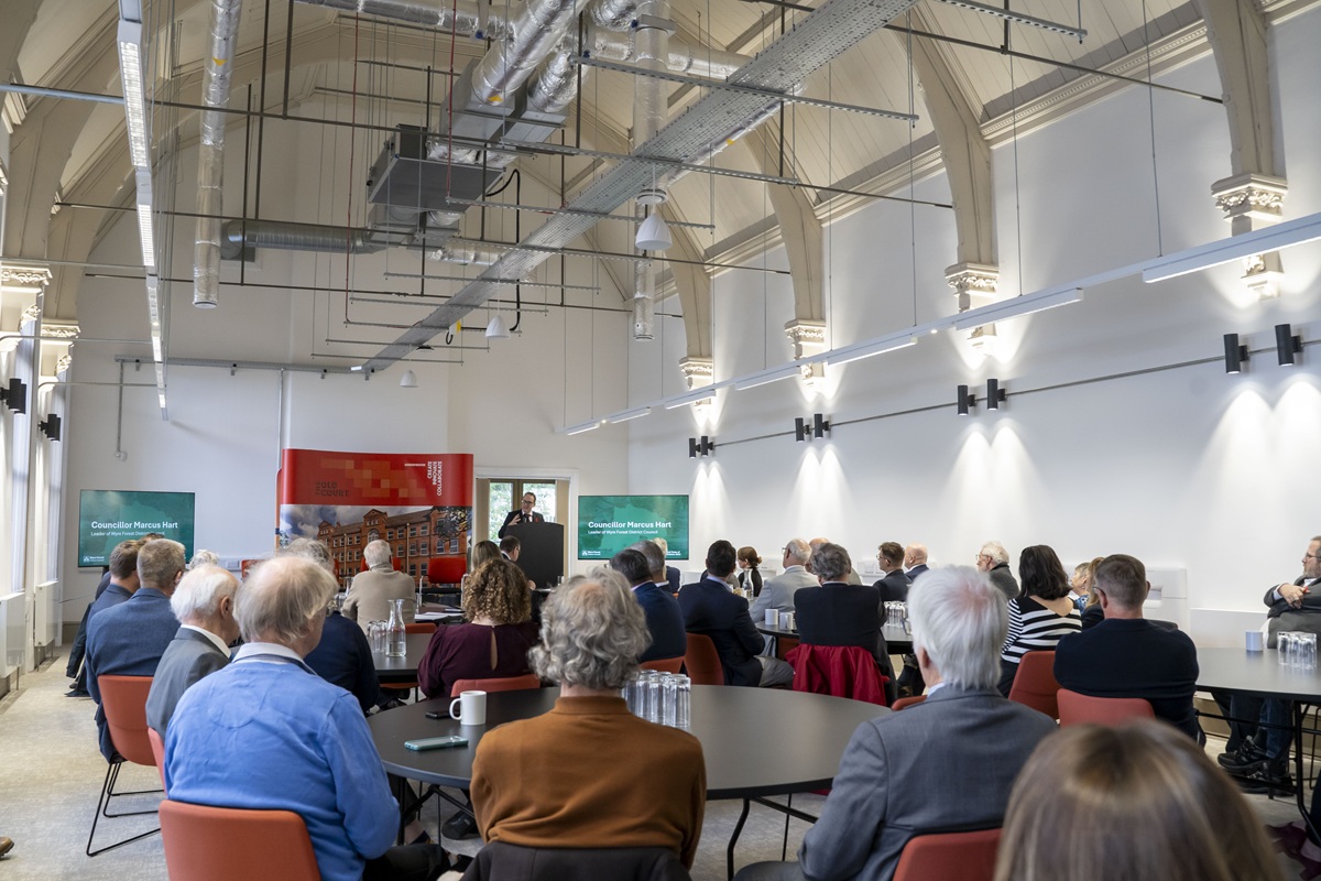 A room full of people sat around tables, listening to a presentation from Councillor Marcus Hart