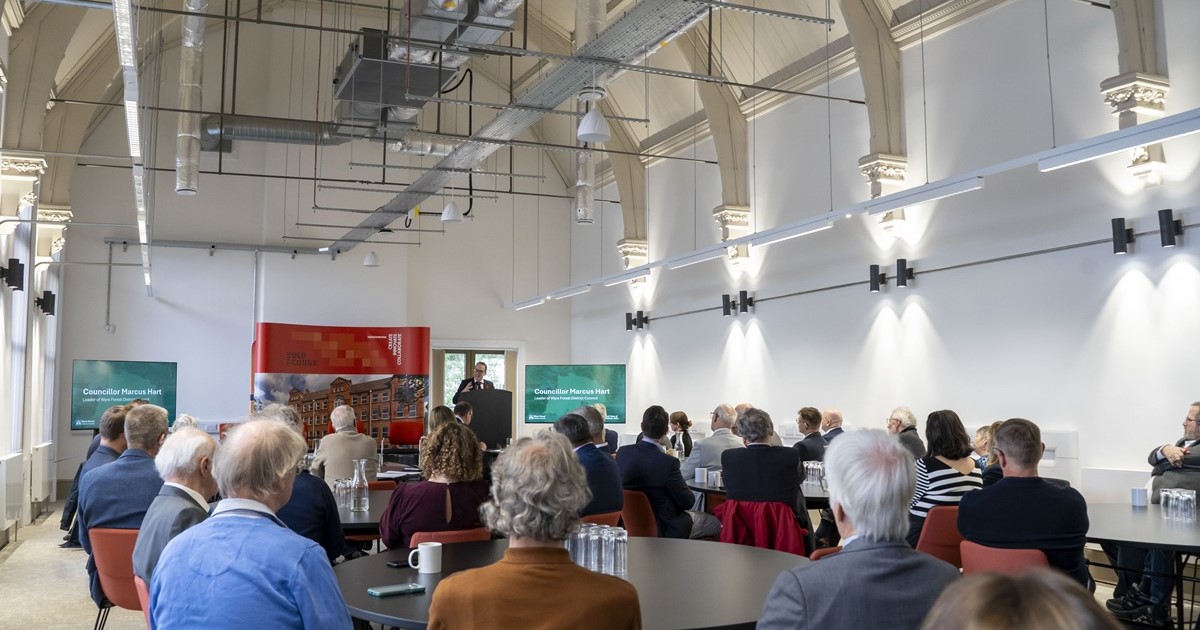 A room full of people sat around tables, listening to a presentation from Councillor Marcus Hart