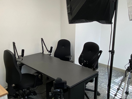 A black table with chairs, a number of microphones are set up