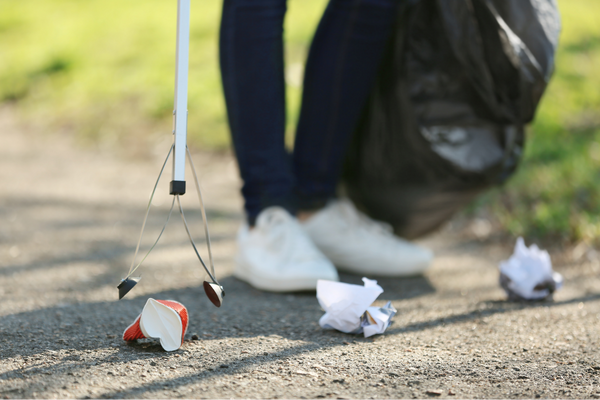 person holding a litter picker and rubbish bag, collecting litter from footpath