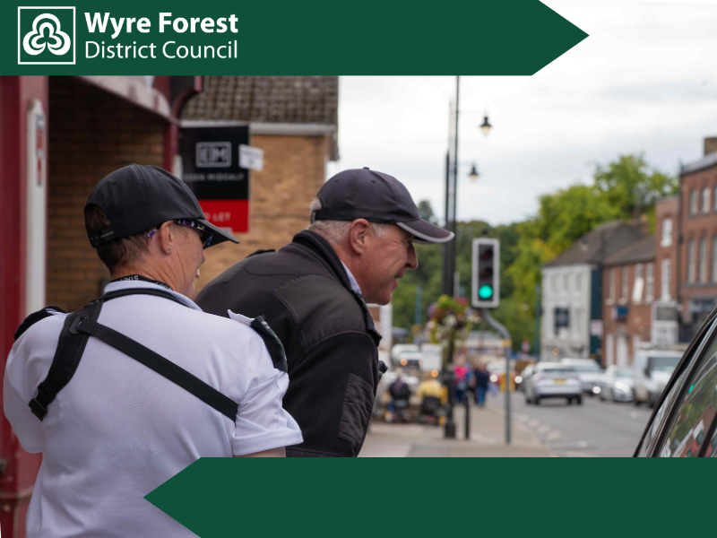 Two Civil Enforcement Officers in a town centre talking to someone in a car