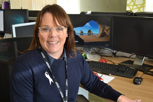 Smiling dark haired woman in glasses sat at desk