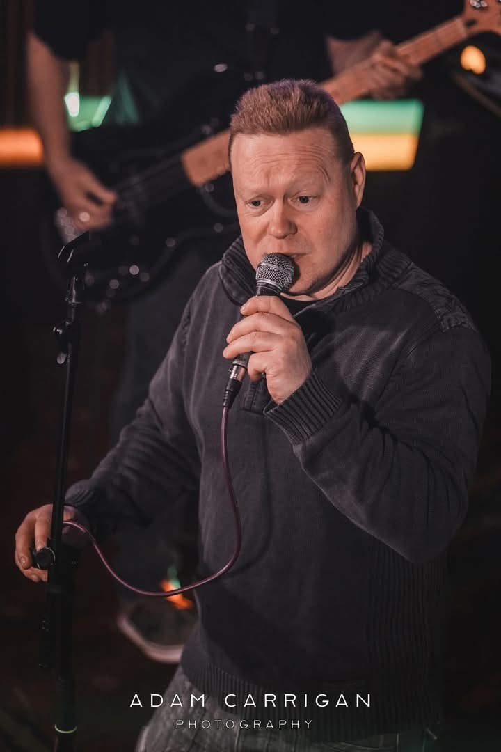  Photo of the lead singer holding a microphone and singing.