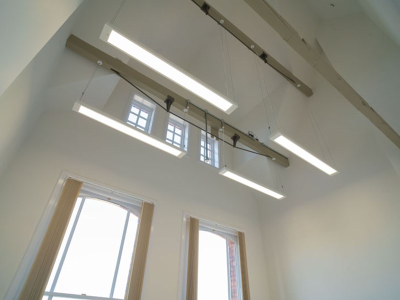 A room with numerous lights and a high ceiling with several windows