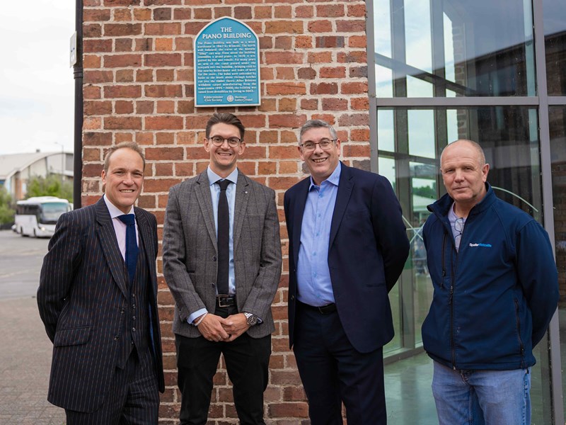 Four males wearing suits, stood outside a grade II listed building with a glass frontage in a town centre