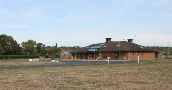 Image of a brick low level building with a car park and grassed area to the front.