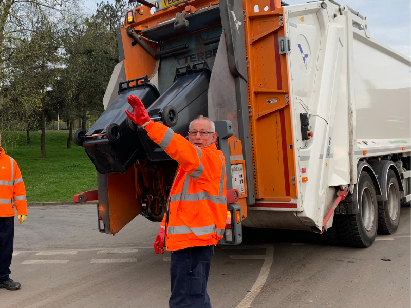 A man in an orange high vis outfit loading a black bin into a waste lorry.